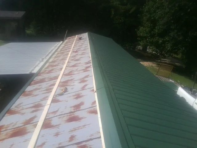 Old rusted panels beside newly installed green metal roofing in Columbia