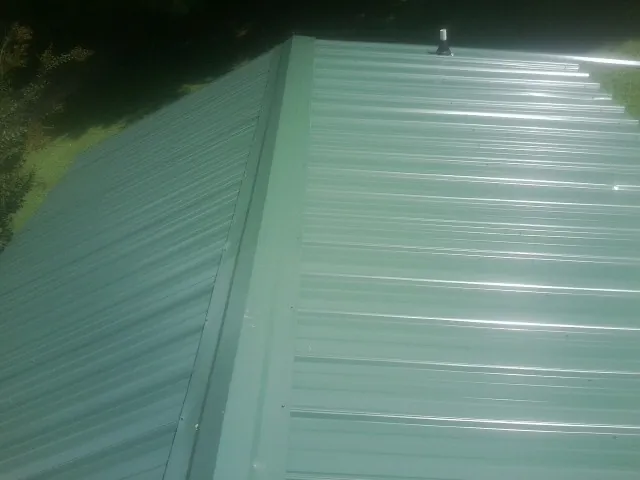 New green metal panels meeting at the ridge of a roof — Flat Roof Repair work by our crew in Columbia