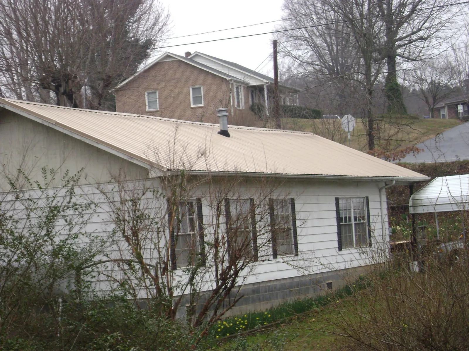 Tan metal roof on a white sided house set into a hillside — Commercial Roofing by Roofing Brothers in Columbia